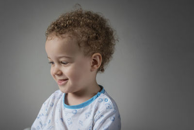 Portrait of smiling boy looking away against gray background