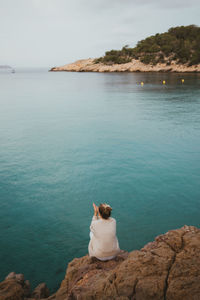 Rear view of woman sitting on rock looking at sea