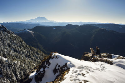 High angle view of man sitting with dog on mountain during winter
