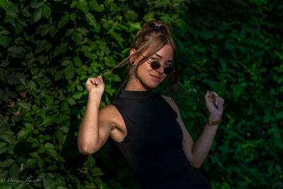 Young woman wearing sunglasses standing against plants