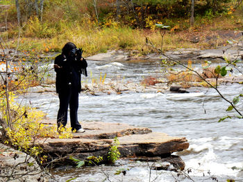 Woman photographing while standing at riverbank in forest