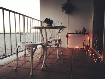 Empty chairs and table by sea against sky