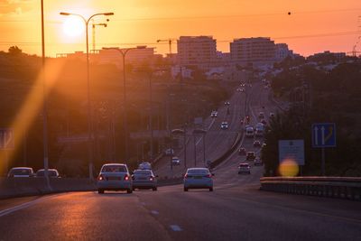 Cars on street against buildings in city at sunset