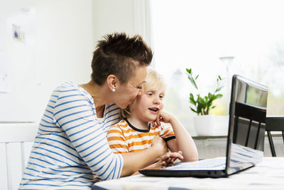 Loving mother embracing boy while using laptop at home