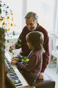 Happy senior man talking to great grandfather playing piano at home