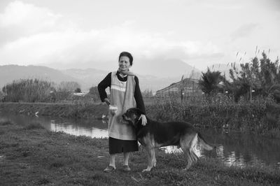 Full length of senior woman with dog standing by lake against sky