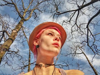 Low angle portrait of woman looking away against bare tree