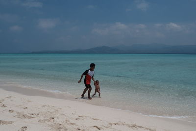 Full length of shirtless on beach against sky