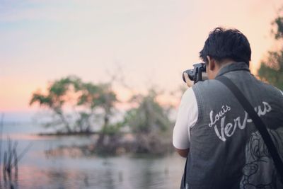 Rear view of man photographing against sky during sunset