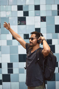 Young man with arms raised standing against wall