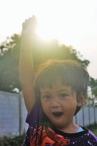 Portrait of cute boy standing with arm raised 