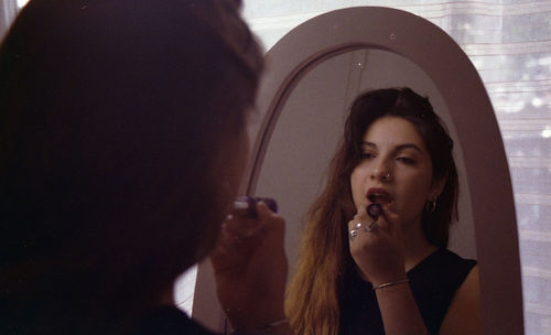 Woman applying lipstick while looking into mirror at home