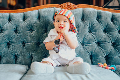 Full length of cute baby boy sitting on sofa at home