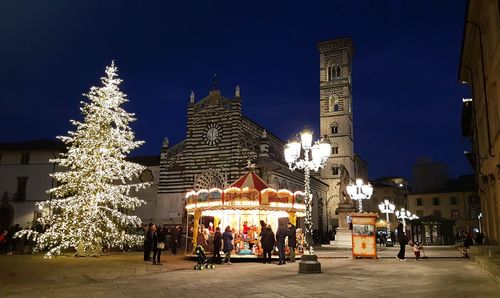 Illuminated christmas tree by buildings in city against sky at night