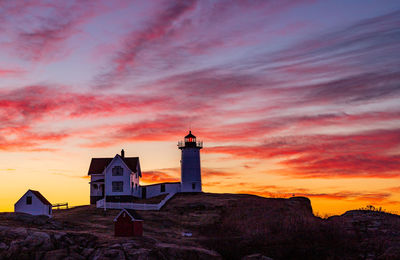 Lighthouse silhouette under a colorful red sky and clouds at sunrise.