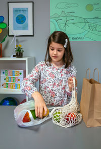 Student taking fruits from disposable plastic bag to reusable mesh bag in ecology classroom