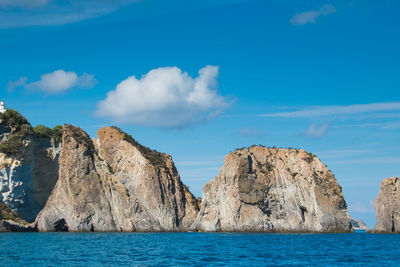 Panoramic view of rocks by sea against blue sky