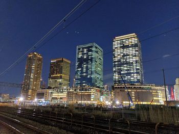 Illuminated railroad tracks by buildings against sky at night