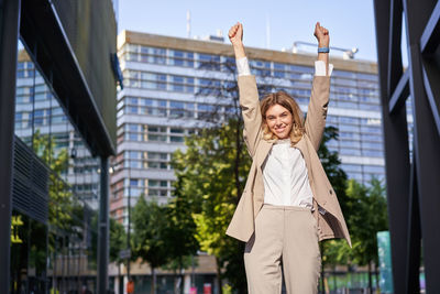 Portrait of young woman with arms raised standing in city