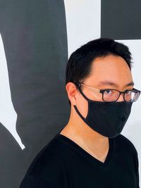 Portrait of young man in eyeglasses and face mask against patterned wall.