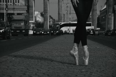Low section of ballet dancer dancing on road in city