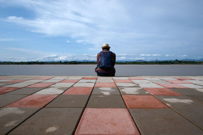 Rear view of woman sitting on tiled floor against sky