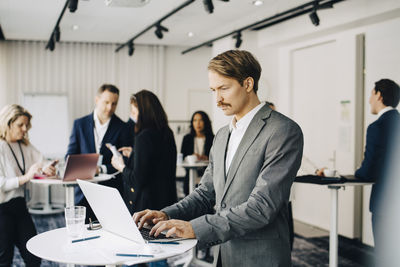 Male business person working over laptop while standing in office seminar