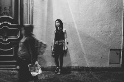 Woman standing against wall in city at night