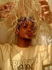 Close-up portrait of young man holding grass against wall