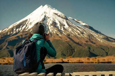 Rear view of woman sitting on snowcapped mountain against sky