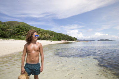 Full length of shirtless man standing at beach against sky