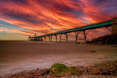 Bridge over sea against orange sky