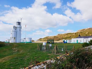 Lighthouse on field by buildings against sky