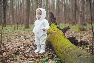 Adorable baby in a bear costume in the forest by a fallen tree