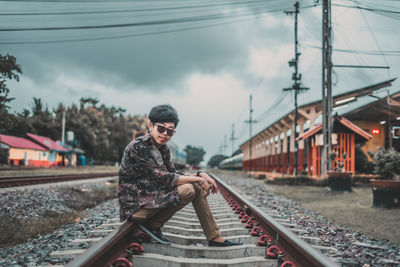 Side view of man sitting on railroad track against sky