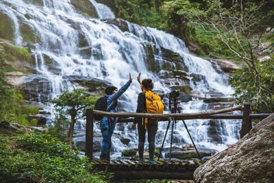 Friends with camera giving high-five by waterfall in forest
