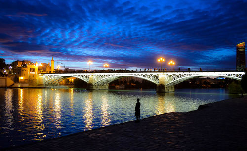 Illuminated bridge over river against sky at night