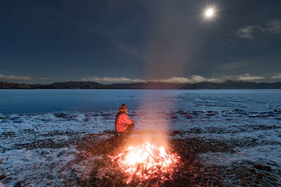 Man by bonfire at beach against sky