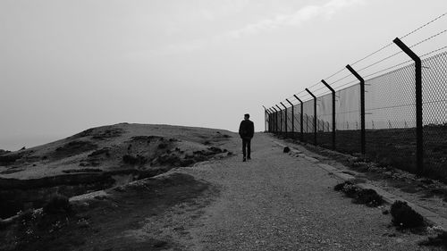 Full length rear view of man walking on dirt road