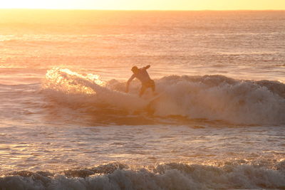 Silhouette man surfing in sea against sky during sunset