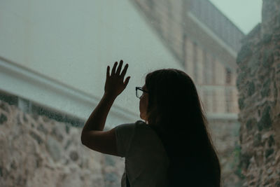 Rear view of woman touching wet window during rainy season