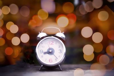 Close-up of alarm clock on table against defocused illuminated lights