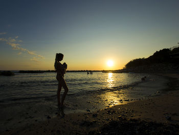 Woman standing on beach against sky during sunset