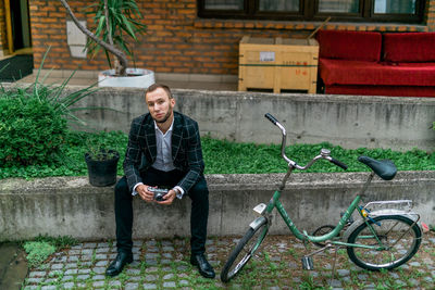 Portrait of young man sitting on bicycle against plants