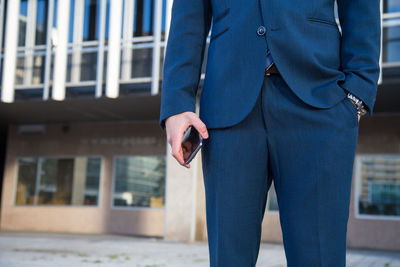 Midsection of businessman holding mobile phone while standing in city