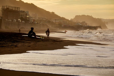 Silhouette people on beach against sky during sunset