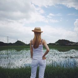 Rear view of man standing on field against cloudy sky