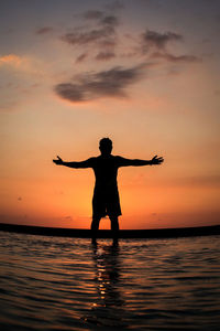 Silhouette man standing on sea against sky during sunset