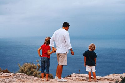 Rear view of men standing by sea against sky