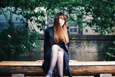 Woman sitting on bench against trees